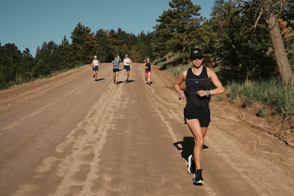woman in black shorts and top running down a dirt road with blue skies in background