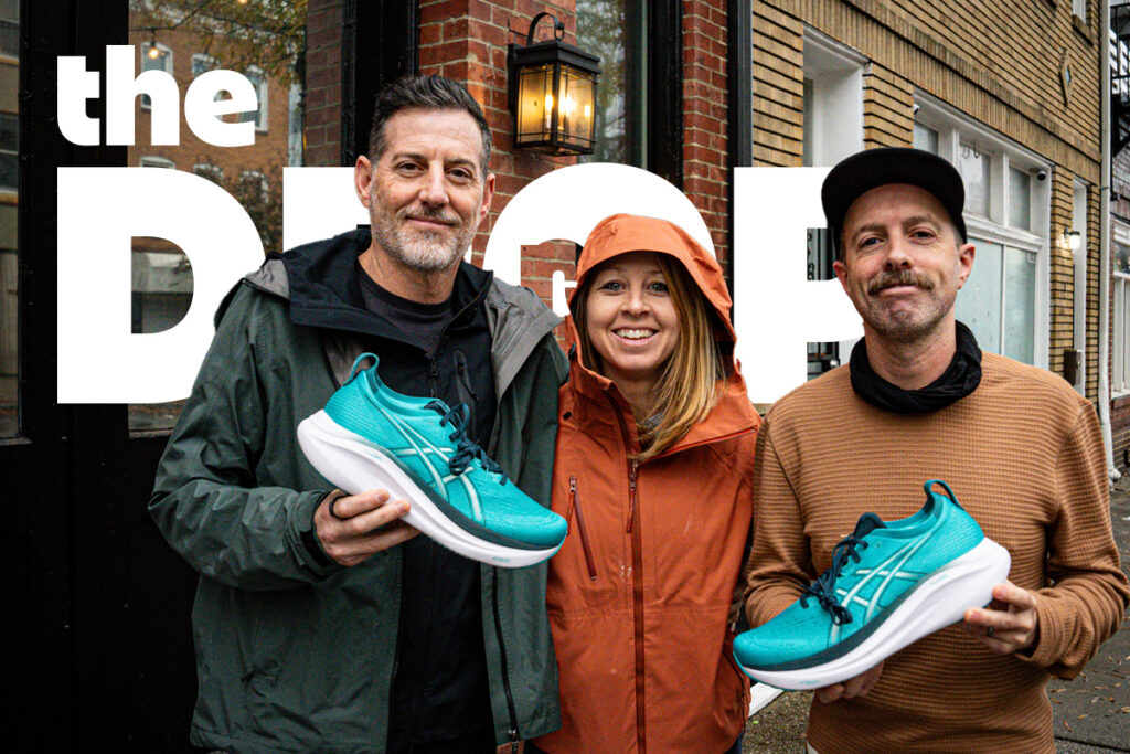 man holding a blue asics running shoe on left, woman in the middle, man holding blue asics running shoe on right