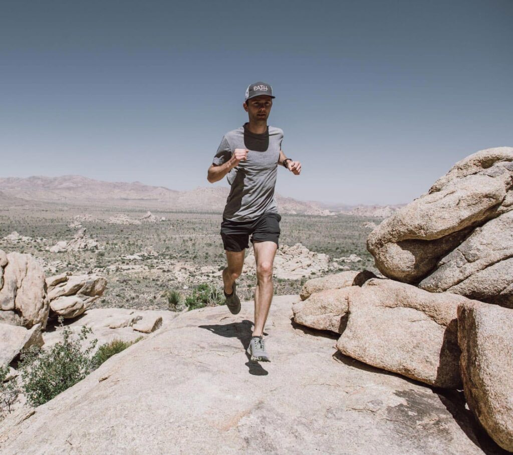 man running on mountain path with sky behind him