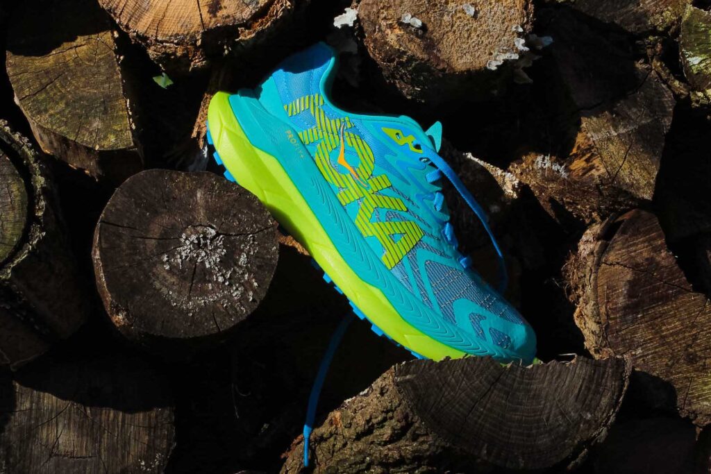 blue hoka trail shoe with yellow midsole on a pile of wood logs