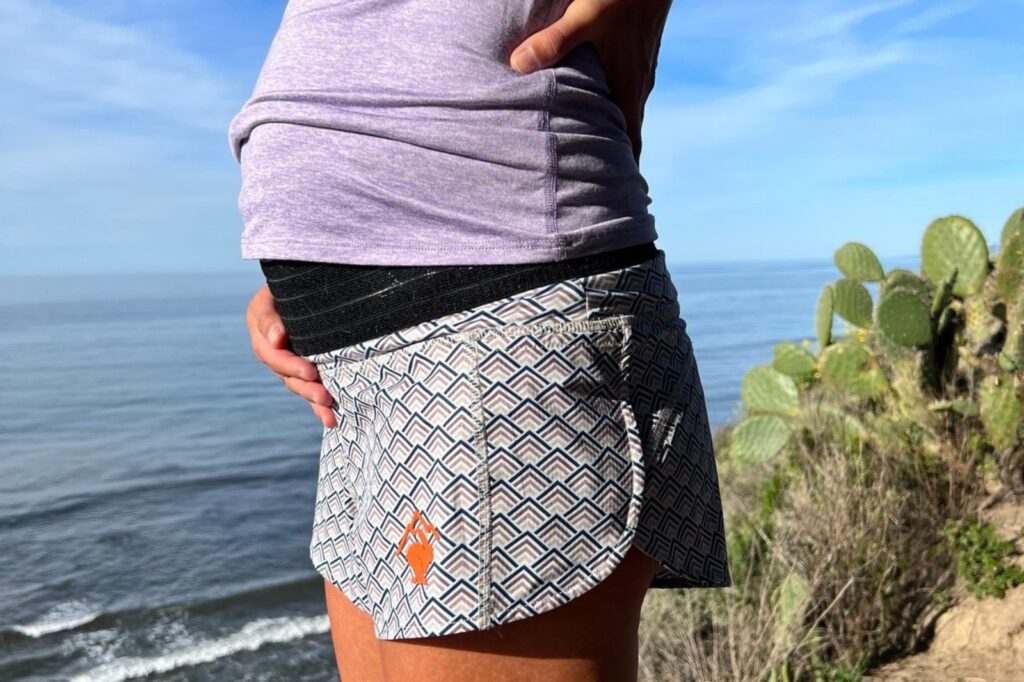 pregnant woman overlooking the ocean with hand on stomach wearing a purple shirt