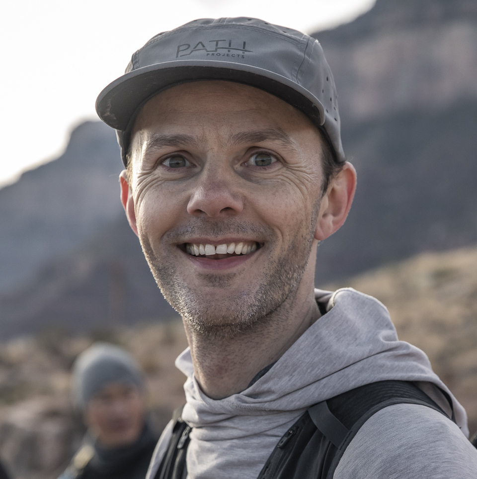 man smiling with a grey baseball cap and grey hoodie