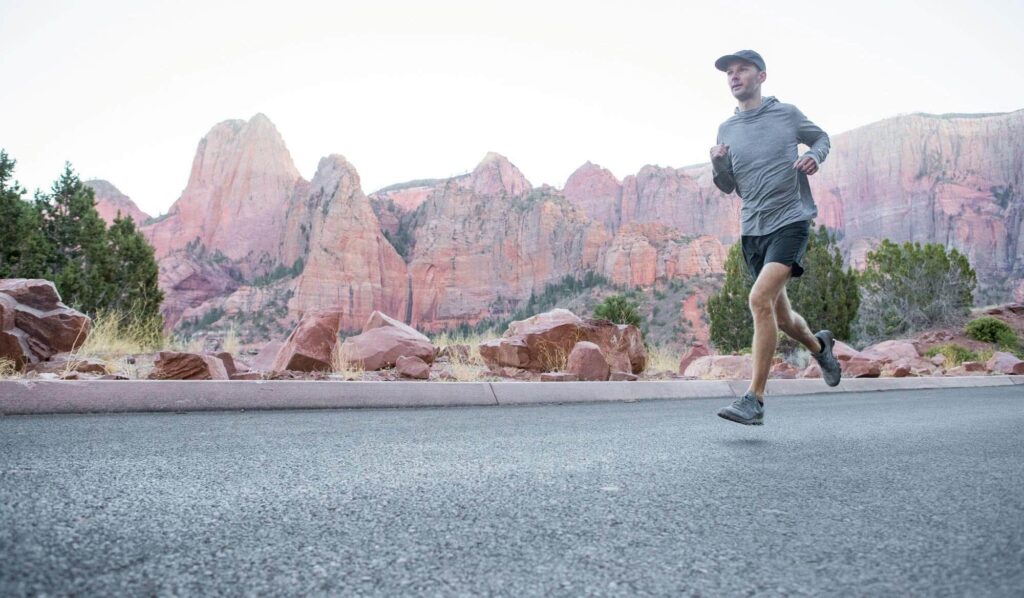 man running on road with red hills behind him