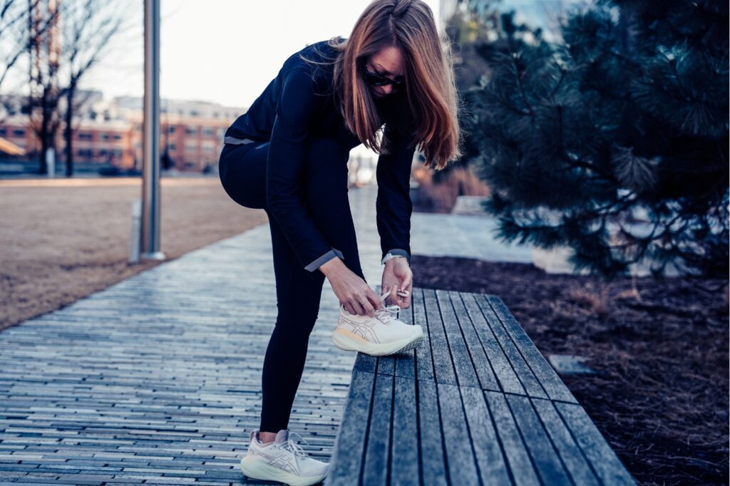 woman tying a running shoe with foot on a bench